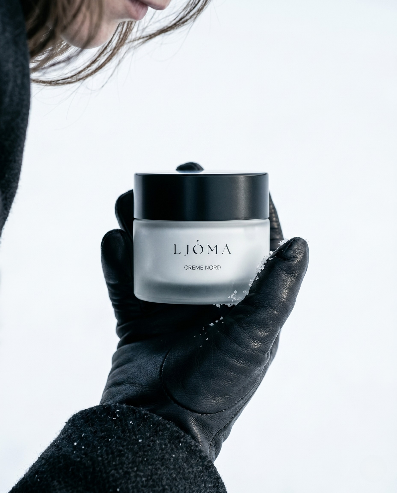 Gloved hand holding a frosted Ljóma Crème Nord jar against snow