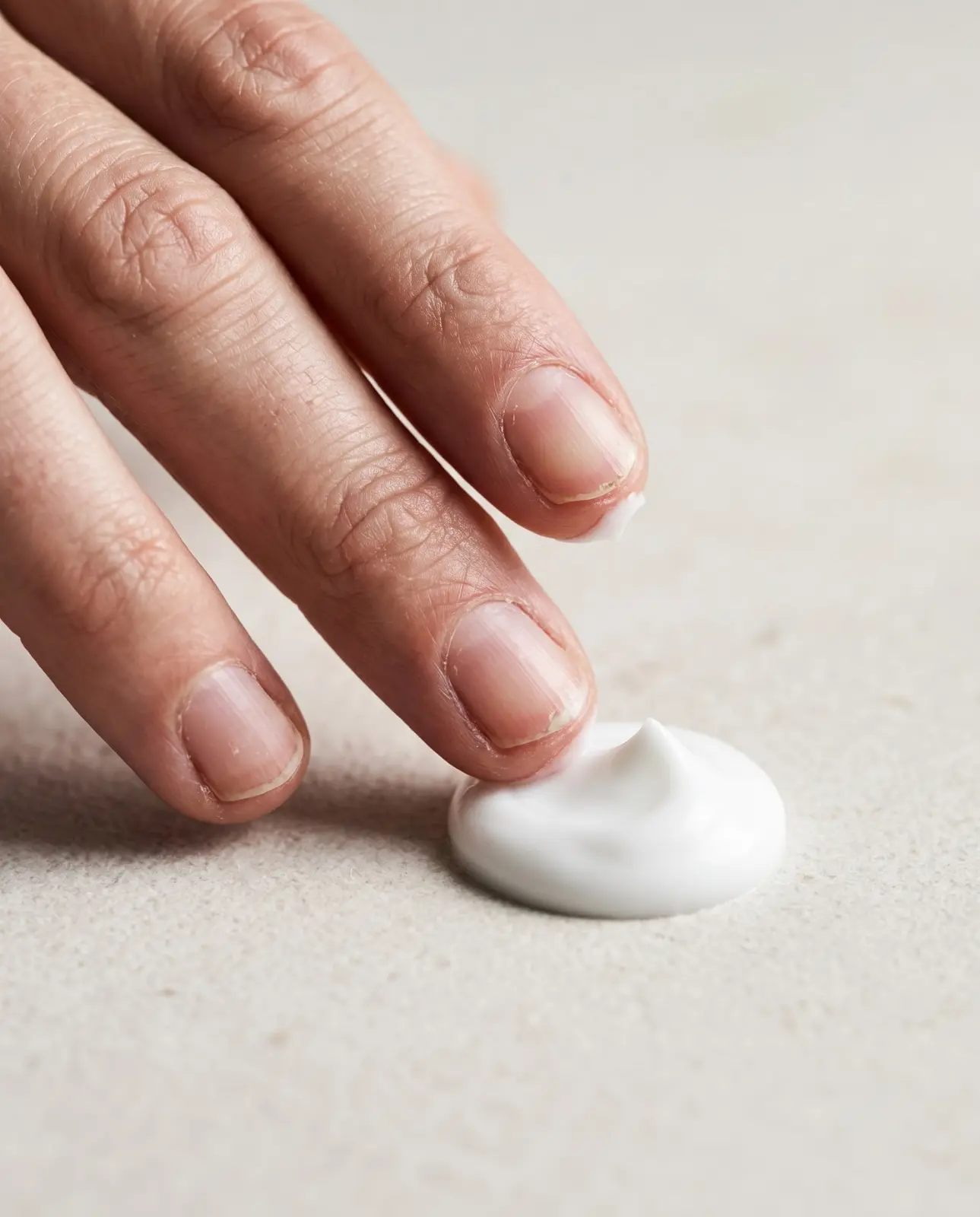 Fingers beside a dab of white cream on stone