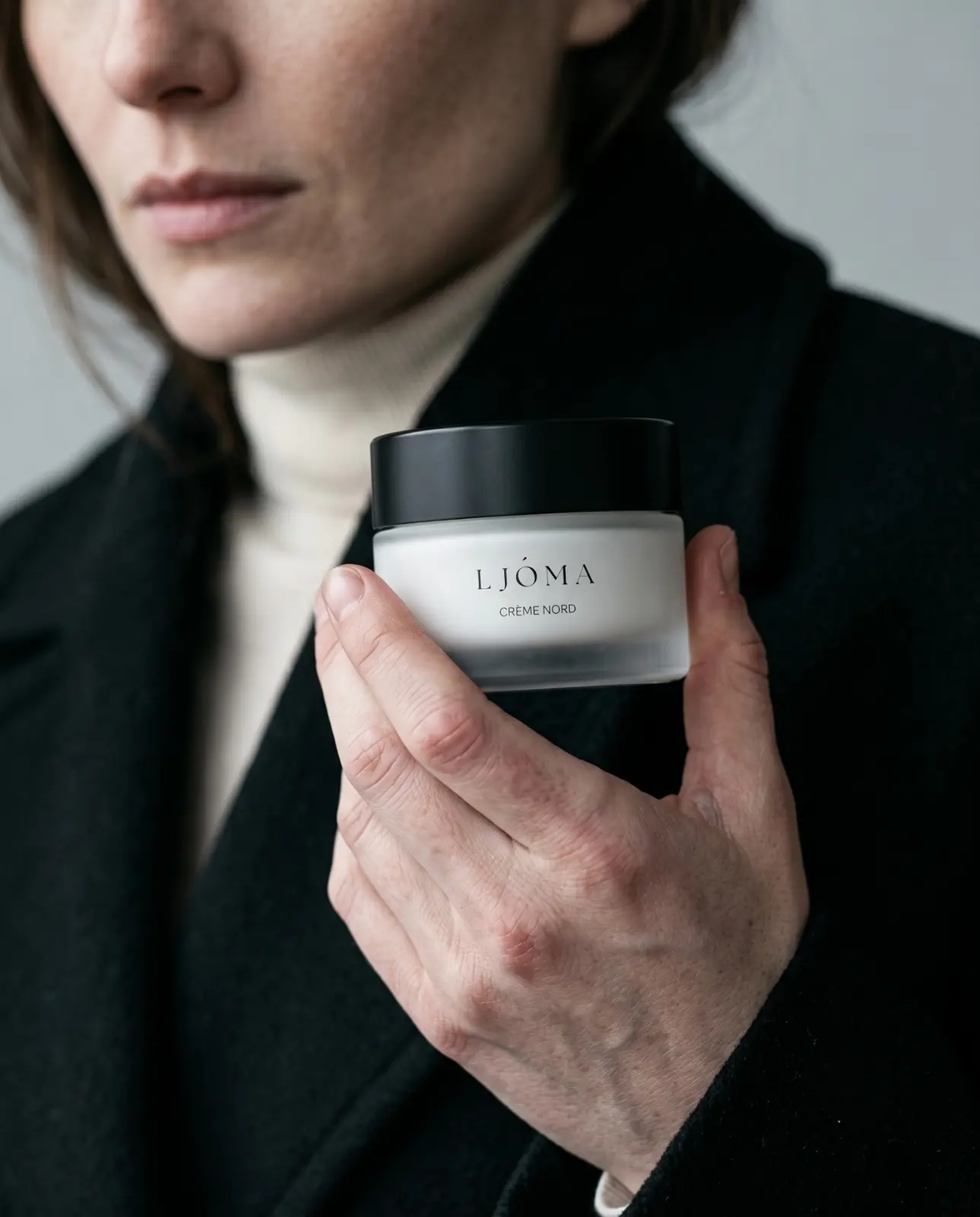 Woman in a dark coat holding the Ljóma Crème Nord jar