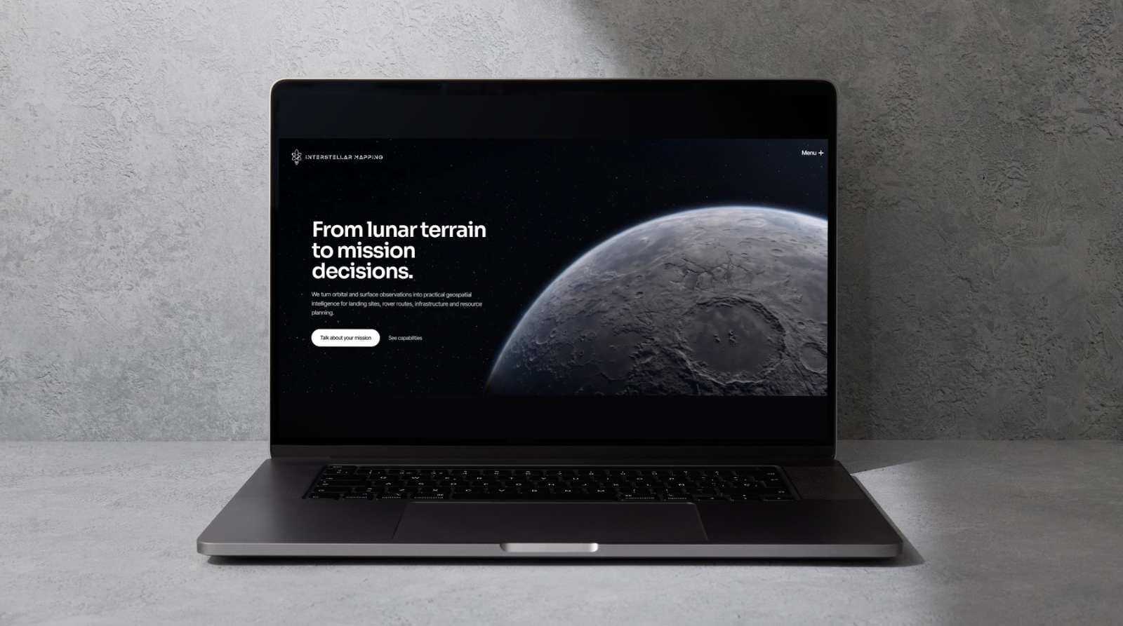 Interstellar Mapping lunar geospatial website displayed on a black laptop against a grey stone wall